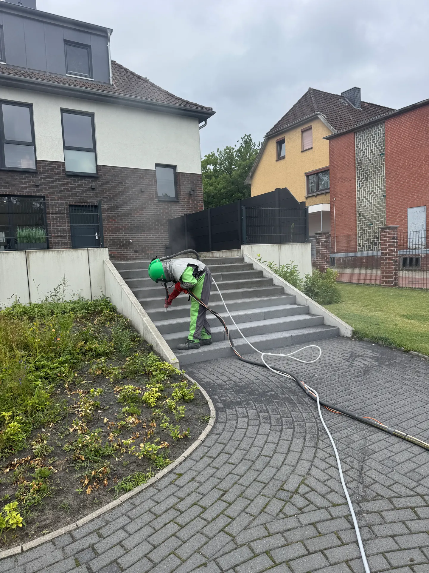 Mitarbeiter in Schutzausrüstung strahlt eine Betontreppe zwischen zwei Stützwänden vor einem Wohnhaus