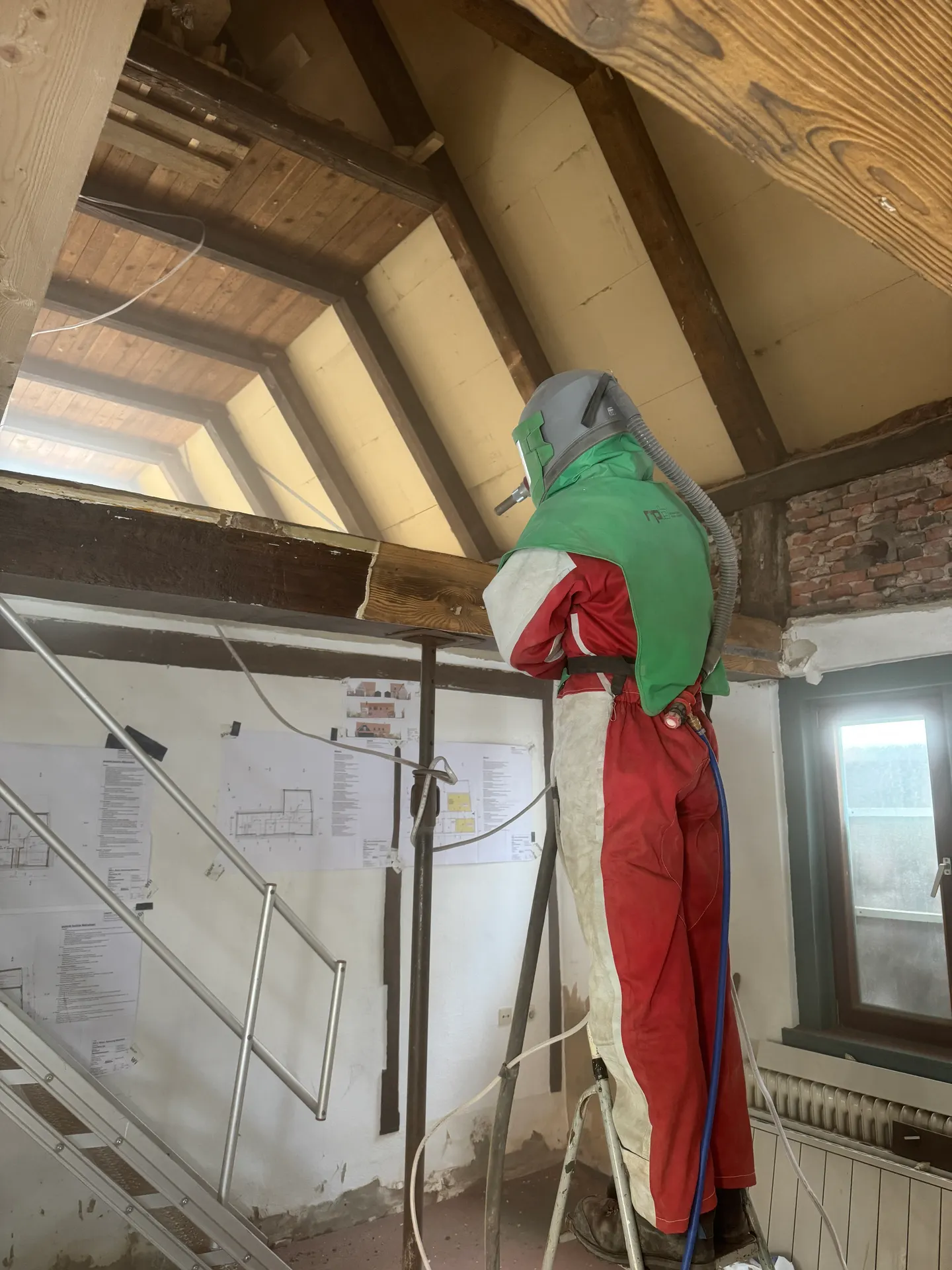 Strahlarbeiten am Fachwerkbalken: links dunkle Beschichtung, rechts hell freigelegtes Holz