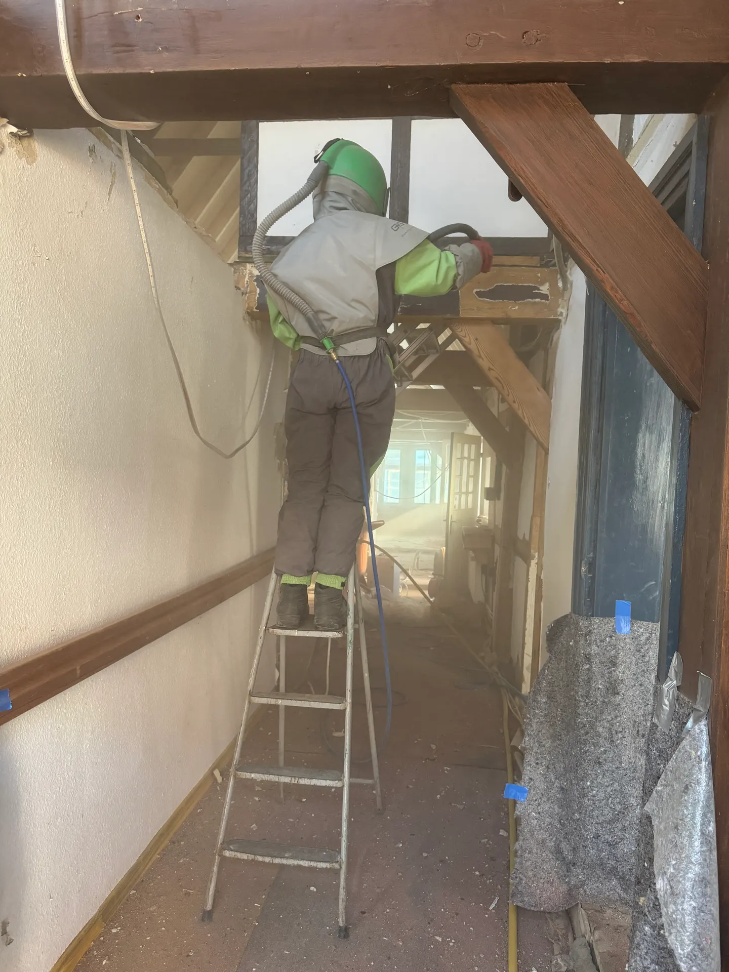 Mitarbeiter auf einer Leiter beim Strahlen von Holzbalken im Fachwerk-Innenraum