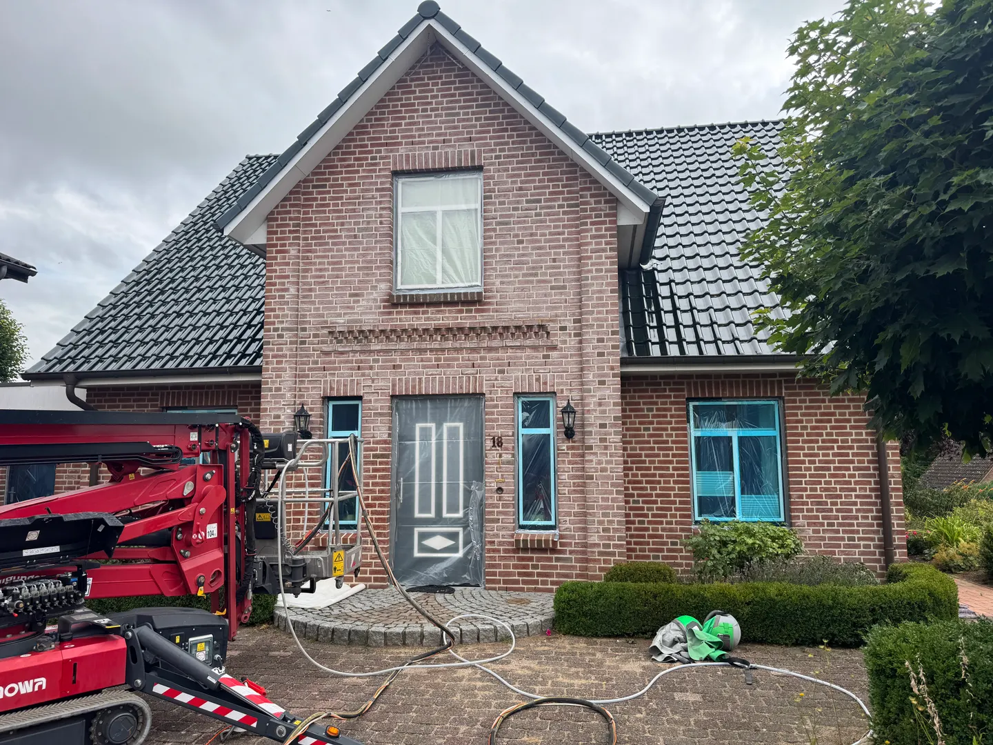 Klinkerfassade eines Einfamilienhauses mit weißen Ausblühungen, Fenster abgeklebt, Hubarbeitsbühne davor