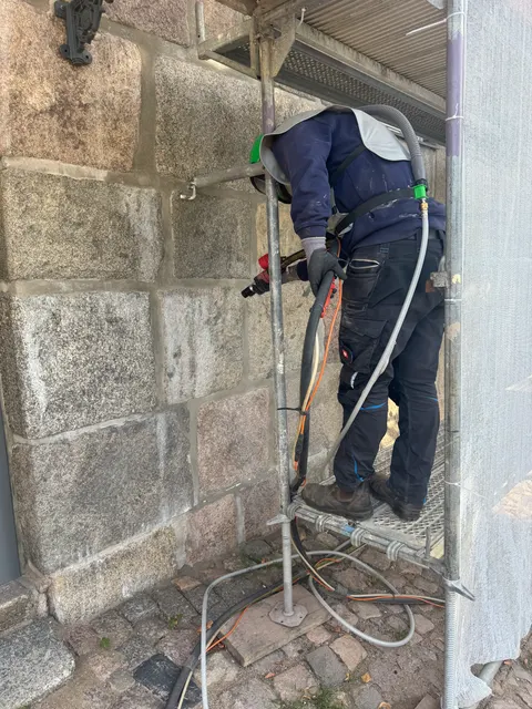 Mitarbeiter auf dem Gerüst beim Feinstrahlen eines Natursteinsockels aus Granitquadern