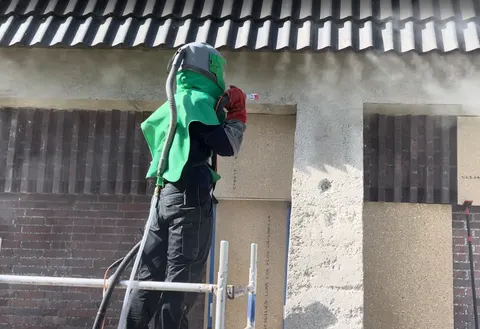 Mitarbeiter auf einem Gerüst beim Strahlen eines Betonpfeilers und Betonsturzes in einer Klinkerfassade